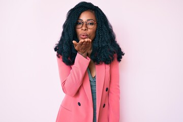 Beautiful african woman wearing business jacket and glasses looking at the camera blowing a kiss with hand on air being lovely and sexy. love expression.