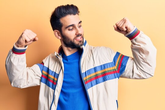 Young handsome man with beard wearing casual jacket showing arms muscles smiling proud. fitness concept.