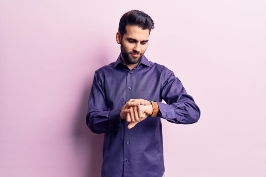 Young handsome man with beard wearing casual shirt checking the time on wrist watch, relaxed and confident