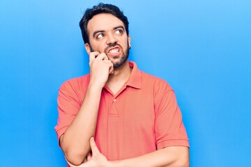 Young hispanic man wearing casual clothes serious face thinking about question with hand on chin, thoughtful about confusing idea