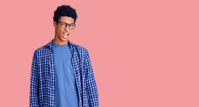 Young african american man wearing casual clothes and glasses winking looking at the camera with sexy expression, cheerful and happy face.