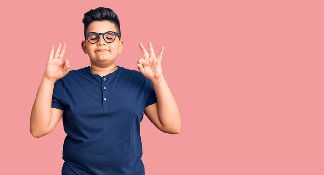 Little Boy Kid Wearing Casual Clothes And Glasses Relax And Smiling With Eyes Closed Doing Meditation Gesture With Fingers. Yoga Concept.