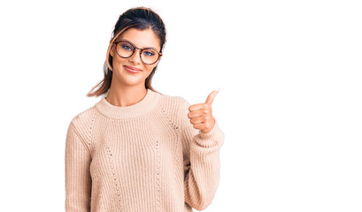 Young beautiful woman wearing casual winter sweater and glasses smiling happy and positive, thumb up doing excellent and approval sign