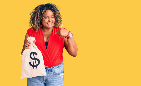 Young african american plus size woman holding money bag with dollar symbol pointing finger to one self smiling happy and proud