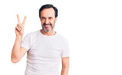 Middle age handsome man wearing casual t-shirt smiling looking to the camera showing fingers doing victory sign. number two.