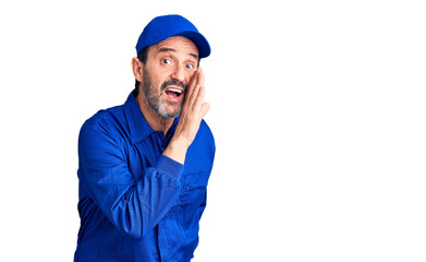 Middle age handsome man wearing mechanic uniform hand on mouth telling secret rumor, whispering malicious talk conversation