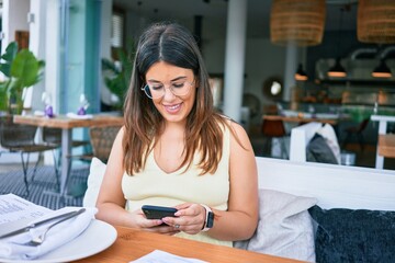 Young beautiful hispanic woman smiling happy. Sitting on the table using smartphone at restaurant