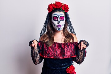 Young woman wearing day of the dead costume over white pointing down looking sad and upset, indicating direction with fingers, unhappy and depressed.