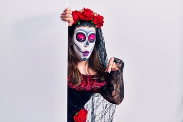 Young woman wearing day of the dead custome holding blank empty banner pointing down with fingers showing advertisement, surprised face and open mouth