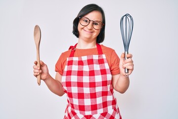 Brunette woman with down syndrome cooking using baker whisk and spoon smiling and laughing hard out...