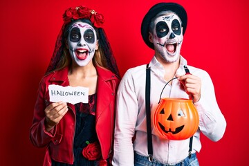 Couple wearing day of the dead costume holding pumpking and halloween paper celebrating crazy and...