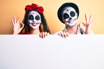 Couple wearing day of the dead costume holding blank empty banner doing ok sign with fingers, smiling friendly gesturing excellent symbol
