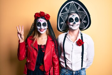 Naklejka na ściany i meble Couple wearing day of the dead costume over yellow showing and pointing up with fingers number three while smiling confident and happy.