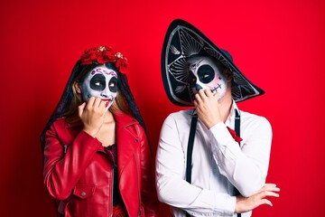 Couple wearing day of the dead costume over red looking stressed and nervous with hands on mouth biting nails. anxiety problem.