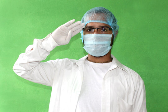 A young doctor in medical uniform with a protective face mask and hand gloves saluting during covid-19, corona virus.