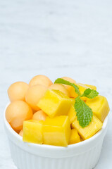 The thai dessert food modern style : The homemade sago in coconut milk with topping is mango cut into squares and cantaloupe ball in the white bowl and placed on tablecloth plaid on the marble table.