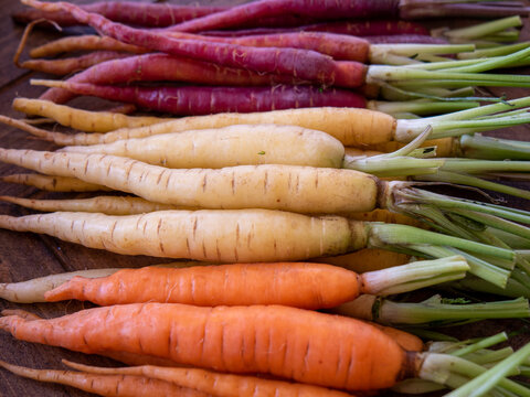 Rainbow carrots with trimmed tops arranged by color on wooden tray in horizontal 
