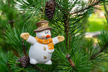 Toy snowman stand on a green branch of a Christmas tree with cones. Merry Christmas and Happy New...