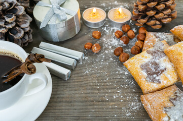 Coffee with pastries, chocolate, and nuts. Festive Christmas decorations, gift, and candles stand on wooden table as a concept for Christmas breakfast