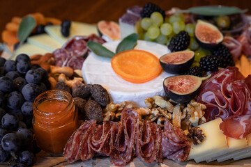 Food board with cured meats prosciutto, salami and coppa, hard and soft cheeses brie, cheddar, gouda, emmental and figs, grapes, blueberries, blackberries, candied orange decorated with sage leaves
