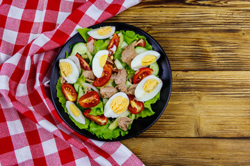 Tasty tuna salad with eggs, lettuce and fresh vegetables on wooden table. Top view