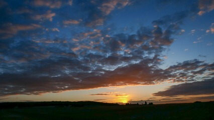 Amazing sunset in the countryside. Cumulonimbus and very colorful stratus in a dramatic sky. Sun disappearing behind a hill.