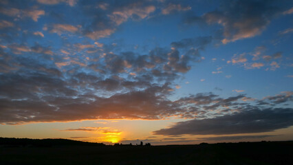 Amazing sunset in the countryside. Cumulonimbus and very colorful stratus in a dramatic sky. Sun disappearing behind a hill.