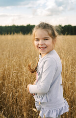 The portrait of a cute small smiling girl in the wheat field. Selective focus. Yellow wheat fied.