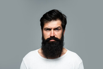 Obraz premium Portrait of confident serious man has beard and mustache, looks seriously, isolated. Hipster guy models in studio. Businessman thinking with expression looking. Handsome male model, closeup face.