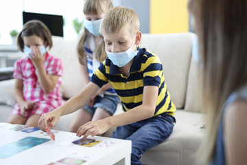 Children in medical protective masks play board games at home. Educational games during coronavirus quarantine concept