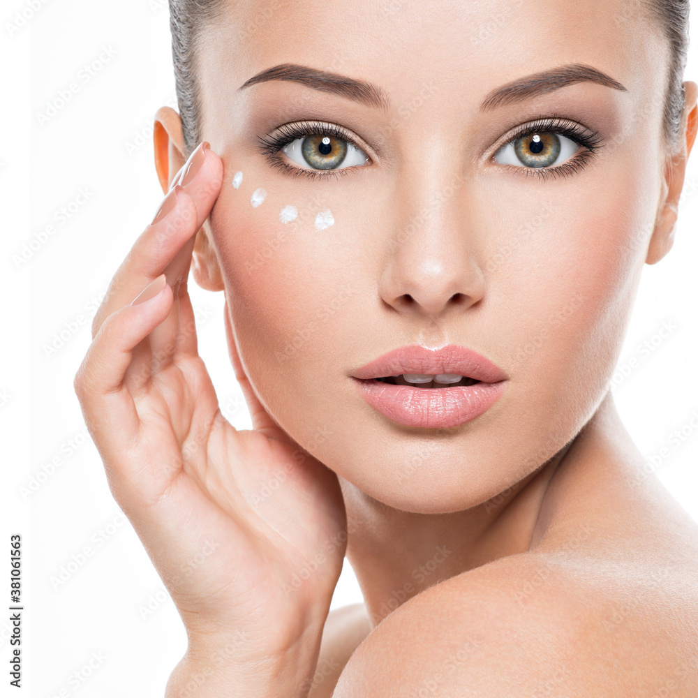 Wall mural woman with healthy face applying cosmetic cream under the eyes