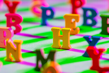 Three-dimensional letters are on table. Multicolored English letters as symbol of children ABC book. English symbols on green background. Concept - teaching to read. All letters except H are blurred. - Powered by Adobe