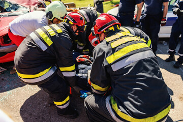 Firefighters taking care of other firefighter and pulling him from crashed car.