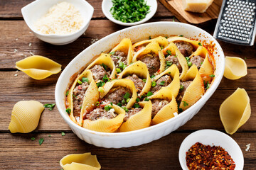 Pasta shells stuffed with minced meat . White baking dish on wooden rustic table.