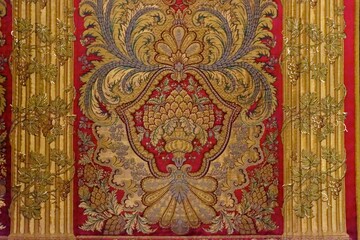 A art on a wall made up of red velvet and several gold elements with golden leaf tied on the golden piller design