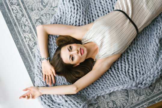 A gorgeous sexy girl in an evening silver ruffled dress lies on a blanket on the floor or on the bed. View of the woman from above