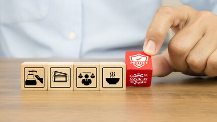 Close-up hand choosing covid-19 protection icon on wooden toy blocks concepts of protect and prevent of coronavirus.