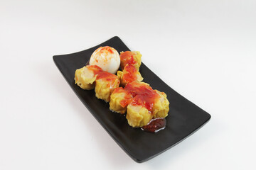 Steamed dimsum dumplings served with egg and chilli sauce on black plate. With white background. isolated  