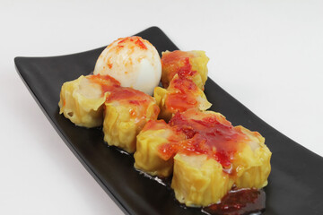 Steamed dimsum dumplings served with egg and chilli sauce on black plate. With white background. isolated  
