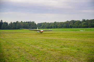a glider is landed on a green grass of  an airdrome field in russian countryside