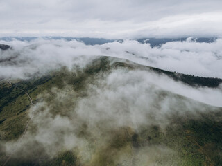 White clouds in the mountains. Clouds are above it and trees on the hill.