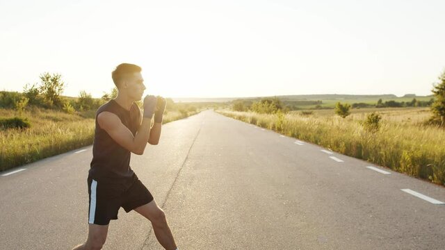 Kickboxer with wrapped hands in tapes training kicks on country road singly