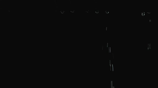 Separate drops of water flow down the black canopy after the rain stops. Close up raindrops dripping in slow motion at night. Bottom view.