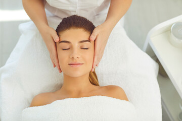 Beautiful woman getting face massage lying with eyes closed on bed in beauty parlor