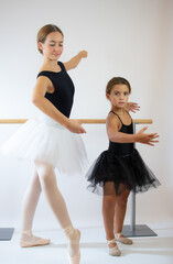 Teacher of the ballet school helps young ballerina perform different choreographic exercises. They rehearse in the ballet class. The teacher communicates with the little girl.