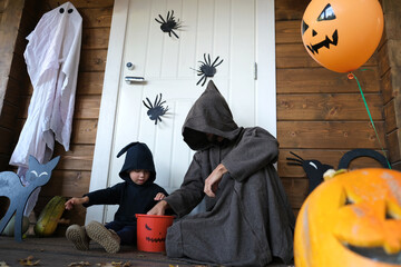 Halloween vibes. Cute child and his father in wizard costumes sitting near house door and looking...