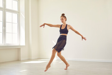 Serious concentrated young female dancer practicing alone in new modern dance studio