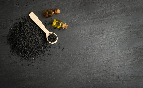 Black cumin oil in small vintage bottle on black stone background. Caraway seeds organic essential oil, tincture, extract, infusion with copy space