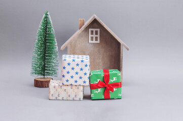 Wooden small house with gifts and Christmas tree against gray background.