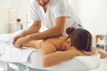 Professional masseur doing body massage for young woman lying on massage table